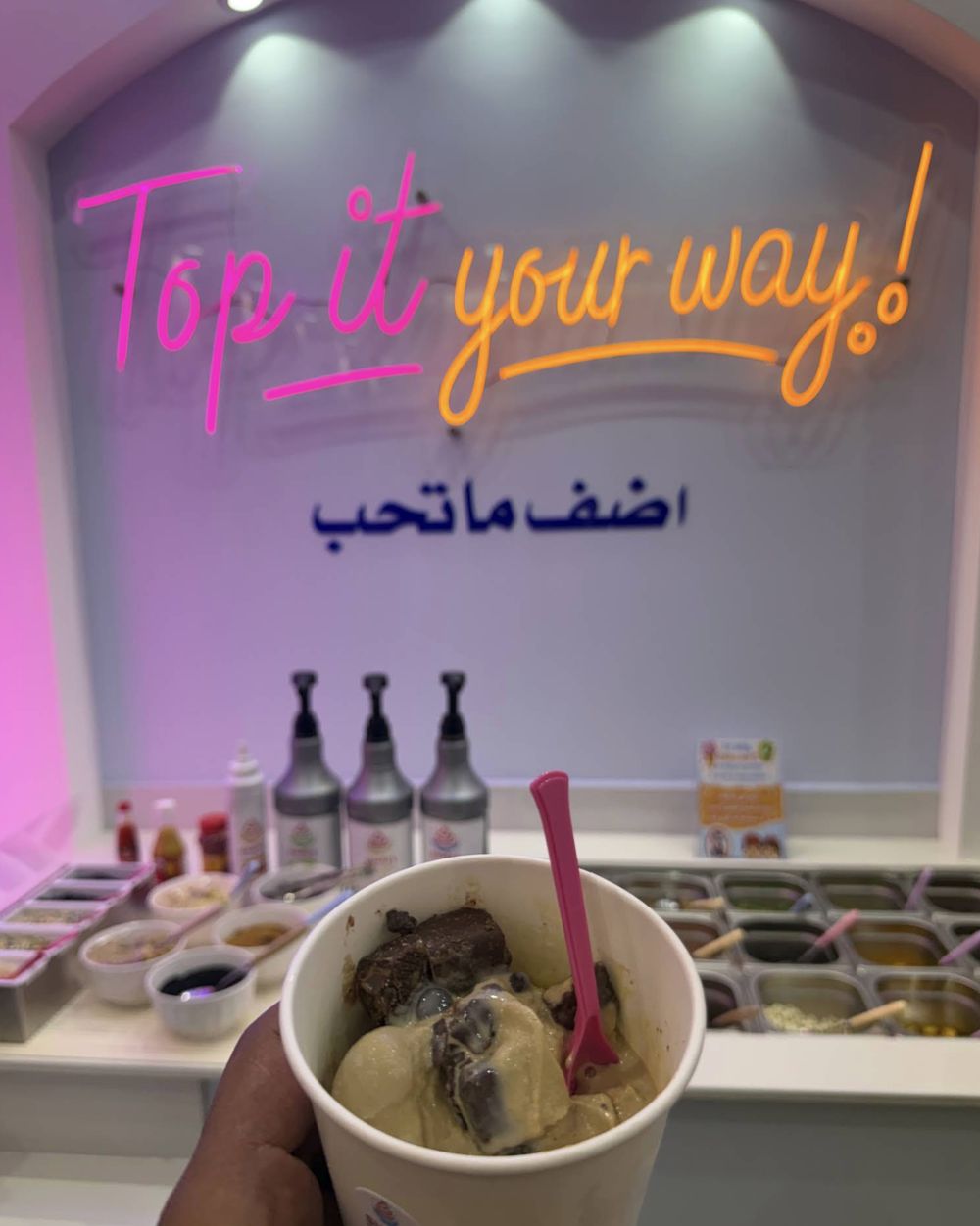 A cup of ice cream under the neon sign that reads Top it your way